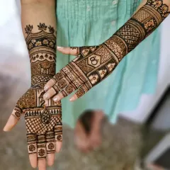 A stylish engagement mehendi with a peacock on one palm and interlocking rings on the other. The design is modern, with a lotus armlet and geometric patterns.