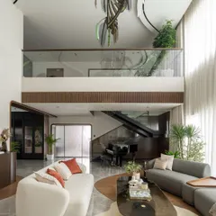 This angle showcases the open and connected layout of the Kolkata home. The living area flows seamlessly towards the den and the upper floor, with curved architectural lines in the mezzanine railing and flooring that guide the eye through the space.