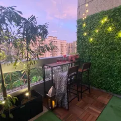 We created this charming bar nook on a small balcony using interlocking wood deck tiles and a patch of artificial grass. The setup is perfect for enjoying the evening, with a vertical garden and string lights adding to the warm, inviting atmosphere.
