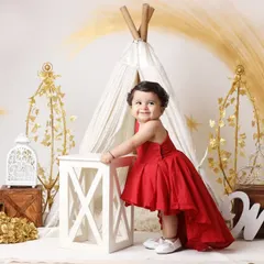 Celebrating a first birthday is a momentous occasion. We create stunning setups like this one, featuring a beautiful red gown and elegant props, to make your little one's milestone portrait truly special.