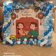 I create custom themed backdrops for any occasion. This setup for Raksha Bandhan includes a large printed banner with festive artwork, framed by a balloon arch in coordinating blue, white, and silver colors, creating a perfect photo opportunity for your event.