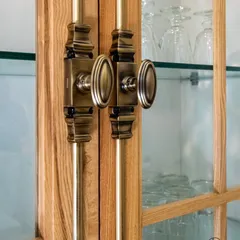 A detailed view of our Cremone Bolt on a glass-fronted kitchen cabinet. This classic hardware adds a layer of vintage charm and mechanical beauty, perfectly complementing the antique brass knobs and pulls used elsewhere in the space.