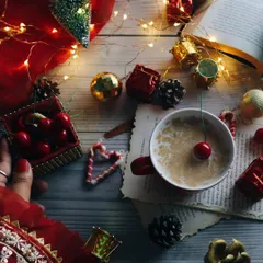A festive Christmas flatlay from above, featuring a red mug, cherries, and various holiday ornaments. This top-down shot captures the busy, joyful clutter of the season.