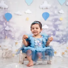 A dreamy first birthday portrait for a little princess, set against a magical sky of clouds and balloons.