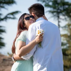 A joyful embrace from behind, with her holding a small bouquet of wildflowers. This shot captures a spontaneous and loving moment.