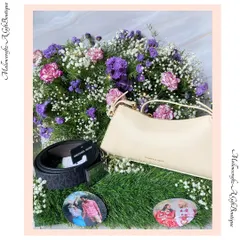 A luxurious anniversary gift featuring a Michael Kors belt and a Charles & Keith handbag, beautifully arranged on a bed of fresh flowers with personalized photo coasters of the couple.
