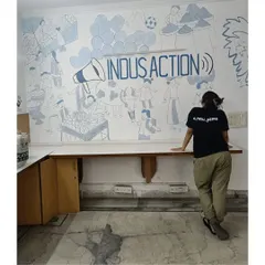 Standing in front of the completed mural project for Indus Action's office. The wall depicts the communities they serve, bringing the heart of their work into their daily space.