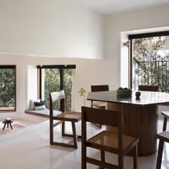 This dining area in our Multilevel House is designed for six. The custom hexagonal dining table and caned chairs sit under a high ceiling with exposed beams, creating an airy and spacious atmosphere for meals.