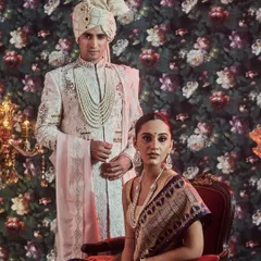 A vision of regal sophistication. Here, we present a coordinated couple's look, featuring a bride in a traditional navy blue Banarasi saree and a groom in an intricately embroidered off-white sherwani with a matching safa.