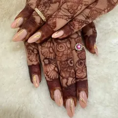 A perfect example of elegant bridal nails. This set features a soft peach base with delicate gold chrome detailing that looks stunning next to intricate mehendi designs.
