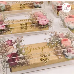 These clear acrylic boxes, personalized with a name in gold and topped with dried flowers, are a modern and elegant way to package wedding favors or small gifts.