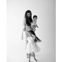 A mother's love in motion. As she holds her baby, her older daughter twirls with joy beside her. This candid black and white photo captures the beautiful, dynamic energy of a family.