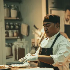 A chef wearing a "Zest" branded cap, carefully preparing food.