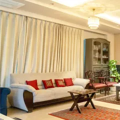 This cozy corner of the living room balances classic and contemporary elements. A neutral sofa is accented with vibrant red cushions, while traditional carved chairs and oriental rugs ground the space in timeless style.