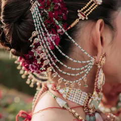 A close up of an intricate bridal bun, adorned with deep red flowers and a multi-layered hair accessory. I focus on creating these detailed updos that not only look stunning but also securely hold the dupatta and jewelry in place.