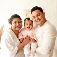 A bright and happy family portrait against a white brick wall. The simple, light-filled setting keeps the focus on the family's joyful expressions.