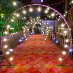 This modern entrance tunnel is constructed with arched frames and exposed bulb lighting. Paired with a decorative patterned carpet, it creates a stylish and well-lit path into the venue, ideal for evening parties and receptions.