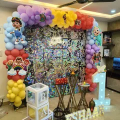 A vibrant Cocomelon themed first birthday party, complete with a colorful balloon arch, a silver shimmer wall, and cutouts of all the favorite characters.