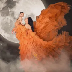 A creative "over the moon" concept for a mother and baby portrait. The flowing orange gown and moon backdrop create a magical and whimsical scene.