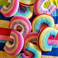 Rainbow heaven. A pile of our cozy and colorful rainbow-shaped cushions, perfect for adding a pop of color and fun to a kid's bed or playroom.