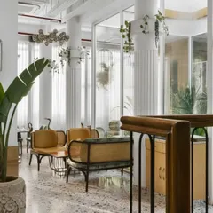 This view showcases the interplay of textures, from the polished terrazzo floor to the fluted white columns and warm wood furniture. Hanging plants and large potted greenery are placed throughout to ensure nature is felt in every corner.
