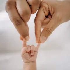 A creative and sweet detail shot, with the parents' fingers forming a heart shape around their baby's tiny hand. A symbol of their endless love.