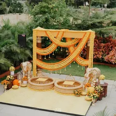 This wider view shows the complete Haldi decor in a beautiful garden setting. The bright yellow and orange marigold garlands stand out against the lush greenery, creating a perfect space for blessings and celebration.