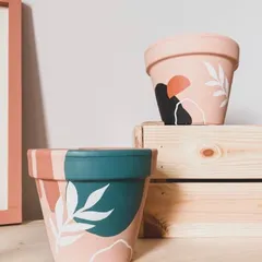 These planters feature abstract botanical designs painted over color-blocked backgrounds. The combination of earthy pinks, deep teals, and leafy whites creates a beautiful statement piece.