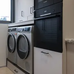 Here, the washer and dryer are placed next to the oven tower. This layout consolidates all the home's "workhorse" appliances into one zone, creating an efficient and practical workflow.