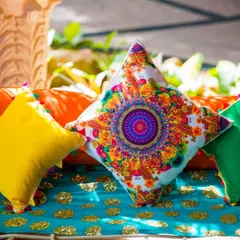 A close-up of colorful and ornate cushions used in a traditional Indian decor setup. The bright patterns and sequins add a rich, festive texture to the seating.