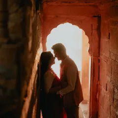 A silhouette of a couple sharing an intimate moment within a stone archway in Jaisalmer. The warm, glowing light creates a romantic and mysterious atmosphere, perfect for a heritage pre-wedding shoot.