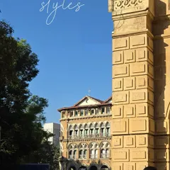 An amalgamation of Victorian, Venetian, and Gothic styles. This shot frames a distant heritage building with a modern stone pillar, showing the layers of architectural history in one view.