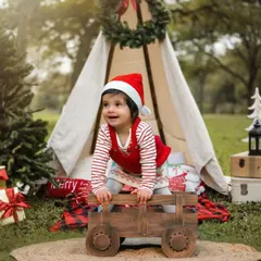 A very merry Christmas shoot. This little one is full of holiday cheer in her Santa hat, enjoying a festive outdoor setup with a teepee and presents.