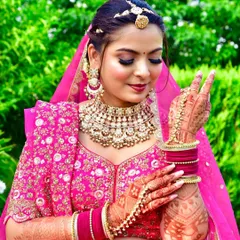 A beautiful outdoor bridal portrait. The bride, dressed in a vibrant pink lehenga, shows off her intricate mehndi with a playful gesture.
