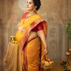 A beautiful solo portrait of an expecting mother in a traditional yellow saree, holding a basket of flowers. Her upward gaze and the artistic backdrop evoke a sense of hope and divine grace.