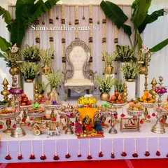 This white and gold themed setup brings a touch of serene elegance to the Seemantha ceremony. The stage is adorned with banana leaves and tuberose flower hangings, complemented by a full 21-plate arrangement on silver stands.