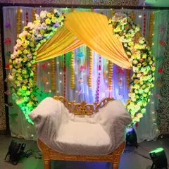 A circular arch backdrop for a Haldi ceremony, decorated with yellow and white flowers. The yellow canopy over the seat and the fairy lights create a bright and cheerful focal point.