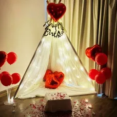 For a unique and intimate celebration, I can set up this beautiful canopy tent in your room. It's adorned with fairy lights, red heart-shaped foil balloons, and scattered rose petals, creating a cozy and romantic corner.