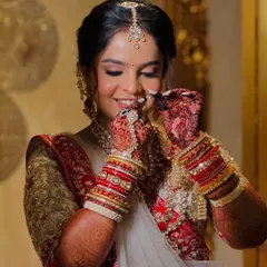 A candid moment of the bride adjusting her nath. This shot captures the intricate details of her jewelry and the soft, glowing makeup that enhances her happy expression.