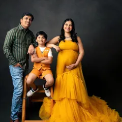 A family growing with love. This studio portrait captures the excitement of a family of three about to become four, with a beautiful flowing gown adding a touch of sunshine to the moment.