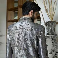 A view of the back of the gunmetal silk sherwani, showcasing the detailed floral threadwork. Every angle is considered to ensure the garment is a work of art from all perspectives.