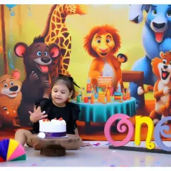 Celebrate your child's first birthday with a wild jungle-themed cake smash. This setup features a vibrant backdrop with cartoon animals and a custom cake.