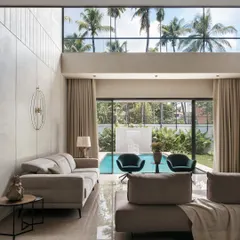 The private family area in Villa Shakthi features a double-height window that frames the tropical view and pool. This space exemplifies our focus on creating luxurious yet comfortable living areas where material richness and natural light converge.