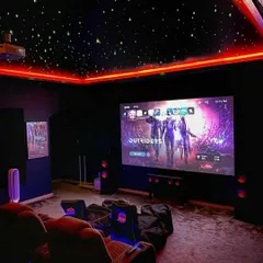 This gaming room uses red RGB perimeter lighting to match the on-screen action. The setup includes a ceiling-mounted projector and a multi-speaker audio system to capture every detail of the game's sound design.