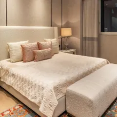 A close-up of the bed styling, with layers of soft textiles in blush and cream tones. The custom headboard and herringbone-patterned wallpaper add subtle texture and sophistication.