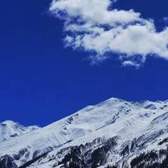 A vast expanse of snow covered mountains under a brilliant, deep blue sky. The stark contrast and the single wisp of a cloud highlight the sheer scale and purity of the high Himalayas.