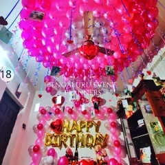 To create an unforgettable birthday surprise, I transformed this entire room with hundreds of pink balloons covering the ceiling. The setup includes 'Happy Birthday' foil balloons and hanging photos for a personal touch that makes the moment truly special.