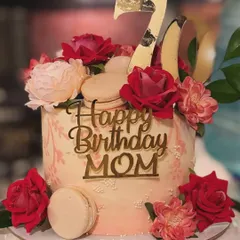 An opulent 70th birthday cake for Mom. This cake is lavishly decorated with red and pink roses, macarons, and a gold "Happy Birthday" topper.