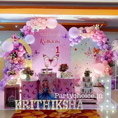 An elaborate butterfly theme for a first birthday celebration. This setup features a large balloon arch in pastel colors, multiple butterfly props, a light-up number '1', and a beautifully decorated cake display area.