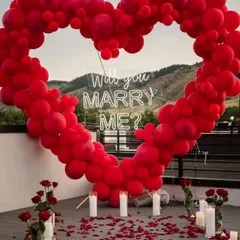 A close-up of the "Will you marry me?" neon sign inside the red balloon heart arch, surrounded by candles and rose petals for a truly romantic proposal setting.